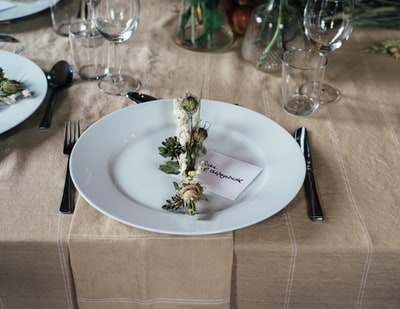 绿色和白色的装饰花放在白色的盘子上，餐具放在桌子上